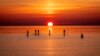 Para pedayung mengarungi Laut Baltik yang tenang di Timmendorfer Strand, Jerman utara saat matahari terbit pada suatu pagi yang dingin (18/4). (Foto: AP)