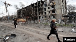 People walk past a residential building, which was heavily damaged in the southern port city of Mariupol, Ukraine during Russia's invasion of Ukraine, April 18, 2022.