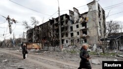 Ljudi prolaze pored stambene zgrade, koja je uništena u južnom lučkom gradu Mariupolju u Ukrajini tokom ruske invazije na Ukrajinu, 18. aprila 2022. 