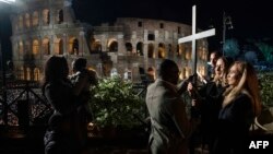 This Vatican Media photo shows Ukrainian nurse Irina (2nd from right), and Russian nurse Albina (R), hand the cross to a family of migrants between the 13th and last Station of the Cross, during the Way of The Cross presided over by the Pope on Good Frida