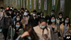 People wearing face masks to help protect from the coronavirus walk by a wall displaying propaganda posters as they head to work at the Central Business District during the morning rush hour, Monday, April 18, 2022, in Beijing. (AP Photo/Andy Wong)