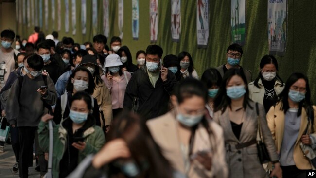 People wearing face masks to help protect from the coronavirus walk by a wall displaying propaganda posters as they head to work at the Central Business District during the morning rush hour, Monday, April 18, 2022, in Beijing. (AP Photo/Andy Wong)