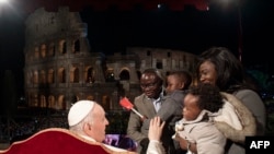 This Vatican Media handout photo shows Pope Francis bless a family of migrants by the Coliseum monument in Rome, during the Way of The Cross presided over by the Pope on Good Friday, April 15, 2022.