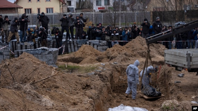 Para petugas menunjukkan warga sipil yang menjadi korban tewas di kuburan massal di Bucha, Ukraina kepada Penuntut ICC dan media, hari Rabu (14/4).