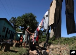 A woman hangs wet clothes drenched by floods, as her son watches, at Clermont in Durban, South Africa, April 14, 2022. Heavy rains and flooding have killed at hundreds of people in South Africa's eastern KwaZulu-Natal province.