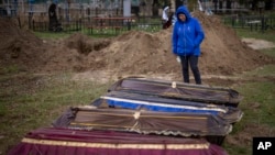 Ira Slepchenko cries next to coffins, one of them holding the body of her husband Sasha Nedolezhko, during an exhumation of a mass grave in Mykulychi, Ukraine, April 17, 2022.