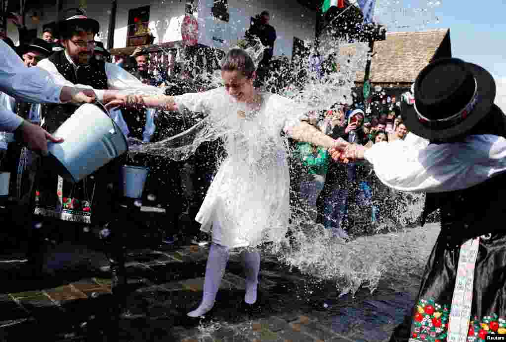 A woman dressed in traditional clothes reacts as men throw water at her during a traditional Easter celebration in Holloko, Hungary.