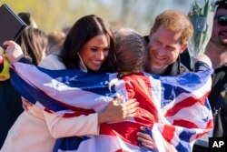 Pangeran Harry dan Meghan Markle, Duke dan Duchess of Sussex, memeluk Lisa Johnston, mantan tenaga medis tentara dan diamputasi, yang merayakan dengan medalinya di venue Invictus Games di Den Haag, Belanda, 17 April 2022. (Foto: AP)