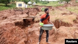 A man collects water near what remains of his home that collapsed while he was sleeping due to flooding in Mzinyathi near Durban, South Africa, April 17, 2022.