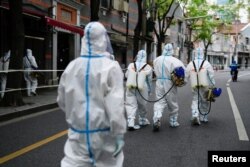 FILE - Workers in protective suits disinfect an old residential area under lockdown amid the coronavirus disease (COVID-19) pandemic, in Shanghai, China, Apr. 15, 2022. (REUTERS/Aly Song)