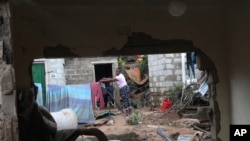 A woman is seen through a damaged wall hanging her clothes on a makeshift washing line in Ntuzuma, outside of Durban, South Africa, Wednesday, April 13, 2022. Flooding in South Africa's Durban area has taken at least 259 lives and is a "catastrophe of enormous proportions," President Cyril Ramaphosa said Wednesday. (AP Photo/Str)