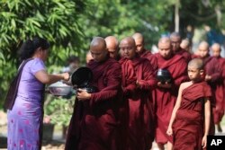 Seorang biksu Buddha menerima sedekah dari seorang umat saat mereka mengumpulkan sedekah pagi pada Kamis, 14 April 2022, di Yangon, Myanmar. (Foto: AP)