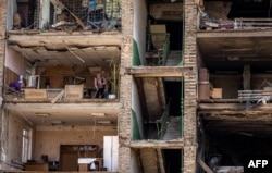 A woman cleans up debris in a building with a collapsed facade after it was hit by overnight Russian strikes, in the town of Vyshneve, in the southwestern suburbs of Kyiv, April 15, 2022.