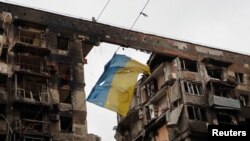 Bendera Ukraina digantung di kawat di depan gedung apartemen yang hancur selama konflik Ukraina-Rusia di kota pelabuhan selatan Mariupol, Ukraina, 14 April 2022. (Foto: REUTERS/Alexander Ermochenko)