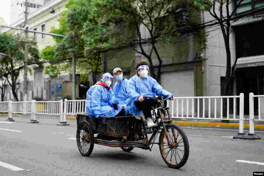 Workers in protective suits ride an electric tricycle during COVID-19 lockdown in Shanghai, China.