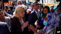 FILE - French far-right leader Marine Le Pen, left, talks to a woman as she campaigns in a market in Pertuis, southern France, April 15, 2022.