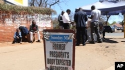 People buy goods from a street vendor near a newspaper banner in Harare, Zimbabwe, Sept, 8 2019. 