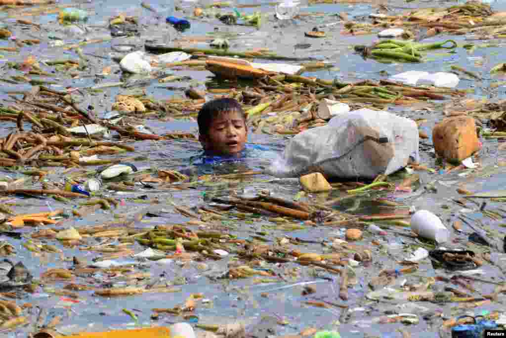 A boy collects recyclable plastic bottles drifting with garbage along the coast of Manila Bay at the slum area in the Baseco Compound in metro Manila, Philippines.