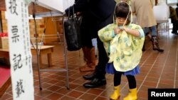 A girl stands next to her father as he fills out his ballot for a national election at a polling station in Tokyo, Oct. 22, 2017. Typhoon Lan is expected to come close to the Japanese capital Monday morning before heading out to sea.