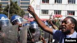 Un policier anti-émeute regarde un manifestant tenant des fleurs dans ses mains pour symboliser la paix à Harare, Zimbabwe, le 17 août 2016.