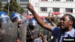 Un policier anti-émeute regarde un manifestant tenant des fleurs dans ses mains pour symboliser la paix à Harare, Zimbabwe, le 17 août 2016.