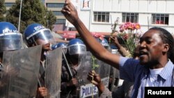 Un policier anti-émeute regarde un manifestant tenant des fleurs dans ses mains pour symboliser la paix à Harare, Zimbabwe, le 17 août 2016.