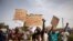 FILE - Demonstrators hold placards in a march to protest the security situation worsening and asking for a response to jihadist attacks, in Ouagadougou, on July 3, 2021. 