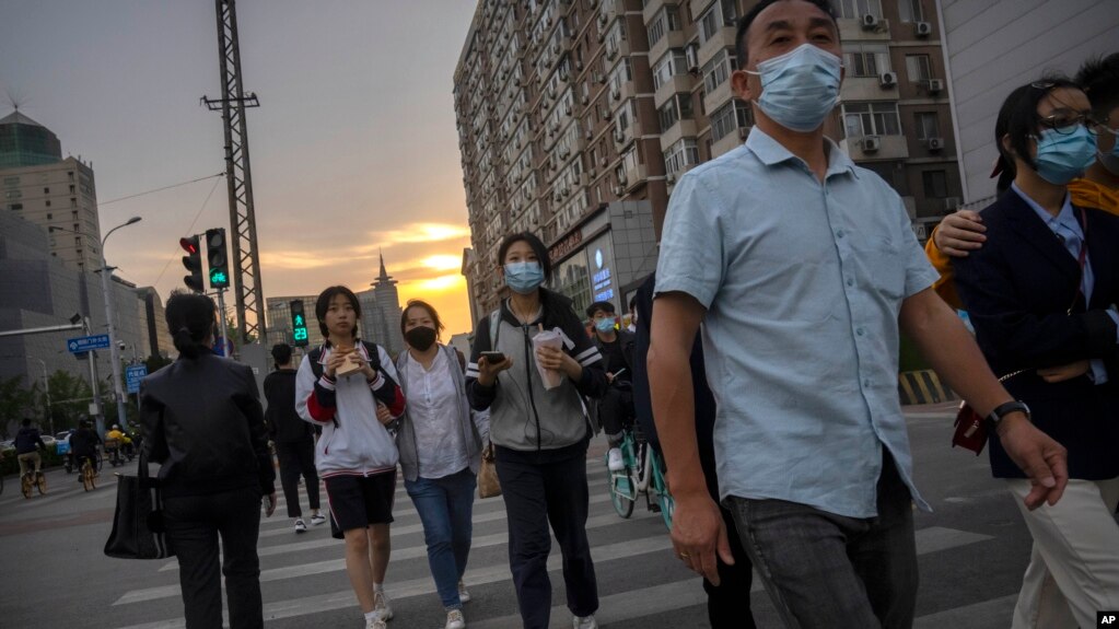 People wearing face masks walk across an intersection during the evening rush hour in Beijing, Wednesday, April 20, 2022. (AP Photo/Mark Schiefelbein)