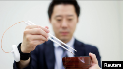 An employee of Kirin Holdings demonstrates chopsticks that can enhance food taste using an electrical stimulation waveform.