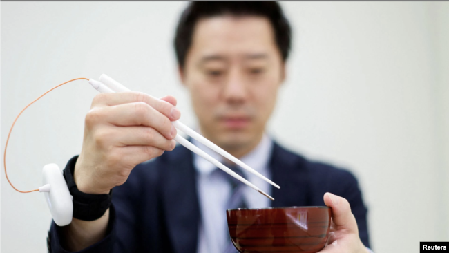 An employee of Kirin Holdings demonstrates chopsticks that can enhance food taste using an electrical stimulation waveform.