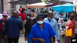 FILE - People wearing face masks walk through the busy Bara Taxi Rank in Soweto, South Africa, April 5, 2022. 