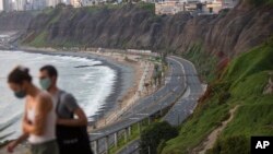 Con una carretera vacía de fondo, Liza Mell, de 26 años, y Jean-Marie Landre, de 27, ambos franceses que viven en Lima, caminan con mascarillas para protegerse del coronavirus, el sábado 21 de marzo de 2020, en Lima, Perú.