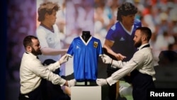 Des artistes posent avec le maillot porté par le footballeur argentin Diego Maradona lors de la Coupe du monde 1986, avant qu'il ne soit mis aux enchères par Sotheby's, à Londres, le 20 avril 2022.