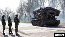 Service members of pro-Russian troops stand next to a combat engineering vehicle, in the southern port of Mariupol, Ukraine, April 20, 2022.