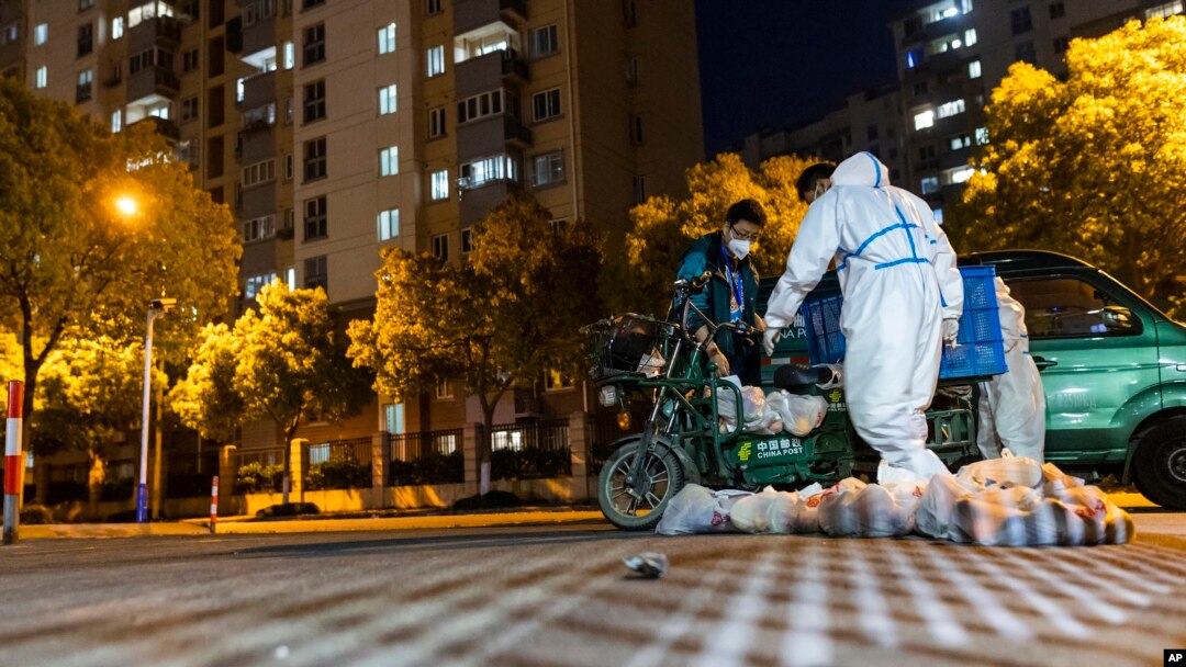 Deliverymen wearing protective suits carry bags of food at the gate of a residential community in Shanghai, China, April 11, 2022.