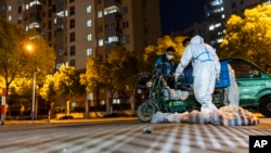 Deliverymen wearing protective suits carry bags of food at the gate of a residential community in Shanghai, China, April 11, 2022. 