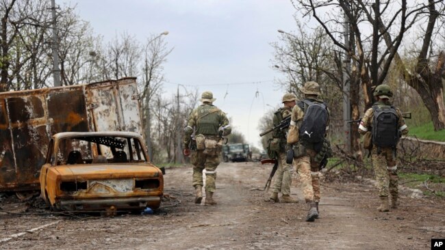 Servicemen of Donetsk People's Republic militia walk past damaged vehicles during a heavy fighting in an area controlled by Russian-backed separatist forces in Mariupol, Ukraine, Apr. 19, 2022.