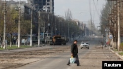 A local resident crosses a street damaged during Ukraine-Russia conflict in the southern port city of Mariupol, Ukraine April 15, 2022.