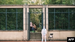 A volunteer wearing personal protective equipment stands as residents line up during a test for the Covid-19 coronavirus in a compound during a Covid-19 lockdown in Pudong district in Shanghai on April 19, 2022.