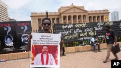 Seorang pengunjuk rasa memegang plakat bergambar PM Mahinda Rajapaksa di dekat kantor presiden di Kolombo, Sri Lanka, 13 April 2022. Poster itu berbunyi "Jatuhkan pemerintah, Ubah sistem." (AP/Eranga Jayawardena)