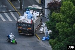 Petugas mengenakan APD memasukkan kotak kosong ke truk terbuka di dekat pintu masuk hunian yang di-lockdown di tengah pandemi COVID-19 di distrik Jing'an, Shanghai, China, 20 April 2022. (Hector RETAMAL / AFP)