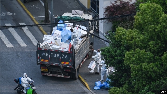 2022年4月20日，穿着防护服的工作人员在上海静安区的一个封闭小区外清理垃圾