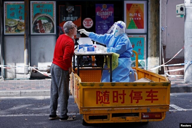 Seorang petugas medis mengenakan APD melakukan tes swab dari seorang penduduk, di tengah wabah COVID-19 di Shanghai, China 22 April 2022. (cnsphoto via REUTERS)