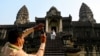 This picture taken on April 8, 2022 shows a guide helping to take a photo of tourists at the Angkor Wat temple complex, a UNESCO World Heritage Site, in Siem Reap province. (Photo by TANG CHHIN Sothy / AFP)