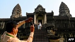 This picture taken on April 8, 2022 shows a guide helping to take a photo of tourists at the Angkor Wat temple complex, a UNESCO World Heritage Site, in Siem Reap province. (Photo by TANG CHHIN Sothy / AFP)