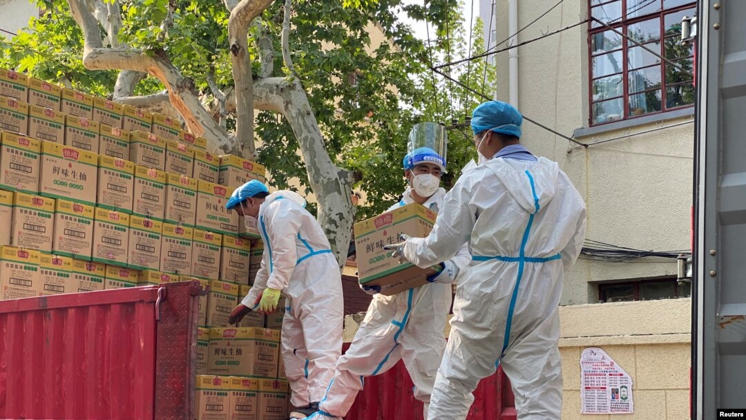 Petugas mengenakan APD menurunkan kotak berlabel kecap dari truk, di tengah wabah COVID-19 di Shanghai, China 21 April 2022. (REUTERS/Andrew Galbraith)