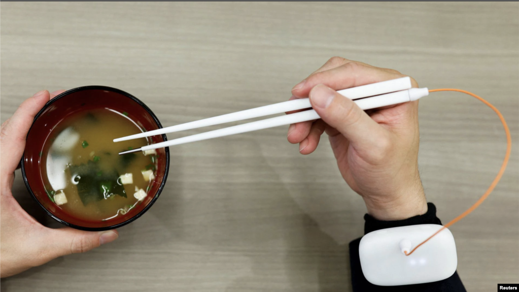 An employee of Kirin Holdings demonstrates chopsticks that can enhance food taste using an electrical stimulation waveform.