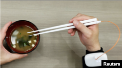 An employee of Kirin Holdings demonstrates chopsticks that can enhance food taste using an electrical stimulation waveform.