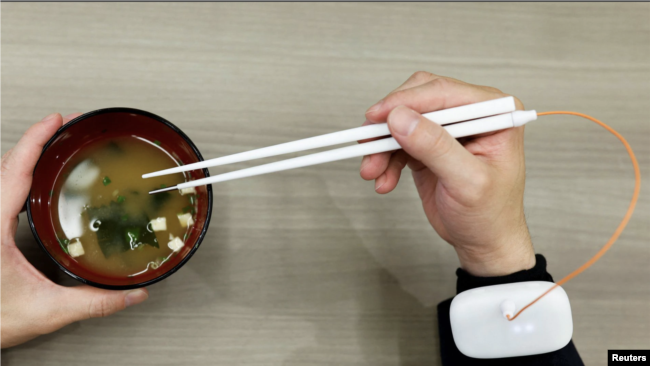 An employee of Kirin Holdings demonstrates chopsticks that can enhance food taste using an electrical stimulation waveform.