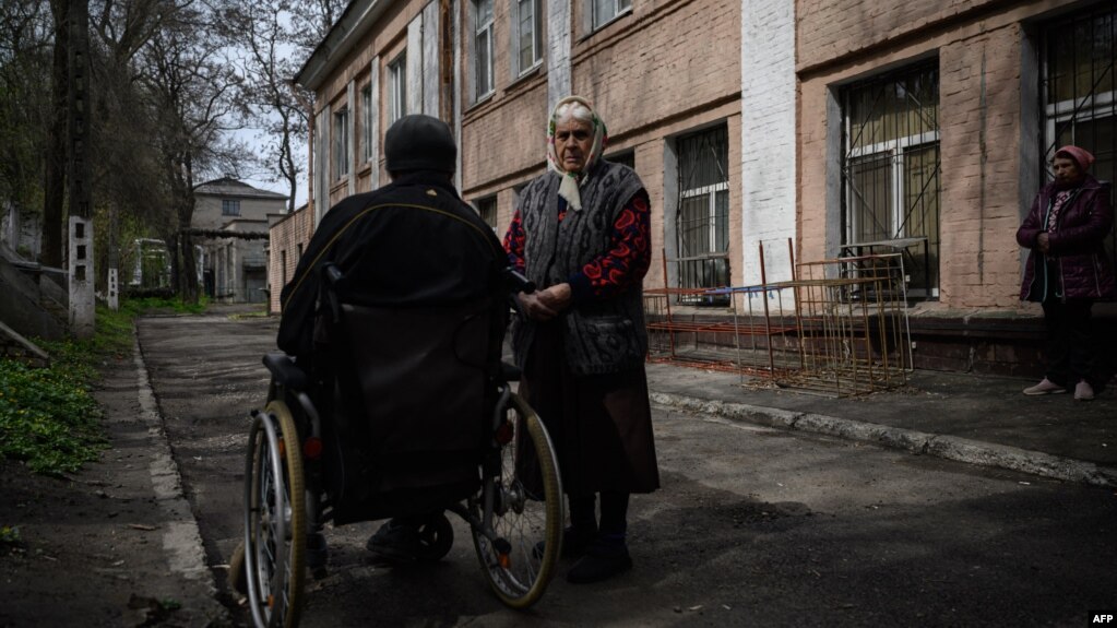 An elderly woman stands beside a man in a wheelchair outside a shelter for internally displaced people, in Dnipro, Ukraine, April 16, 2022. (Photo by Ed JONES / AFP)